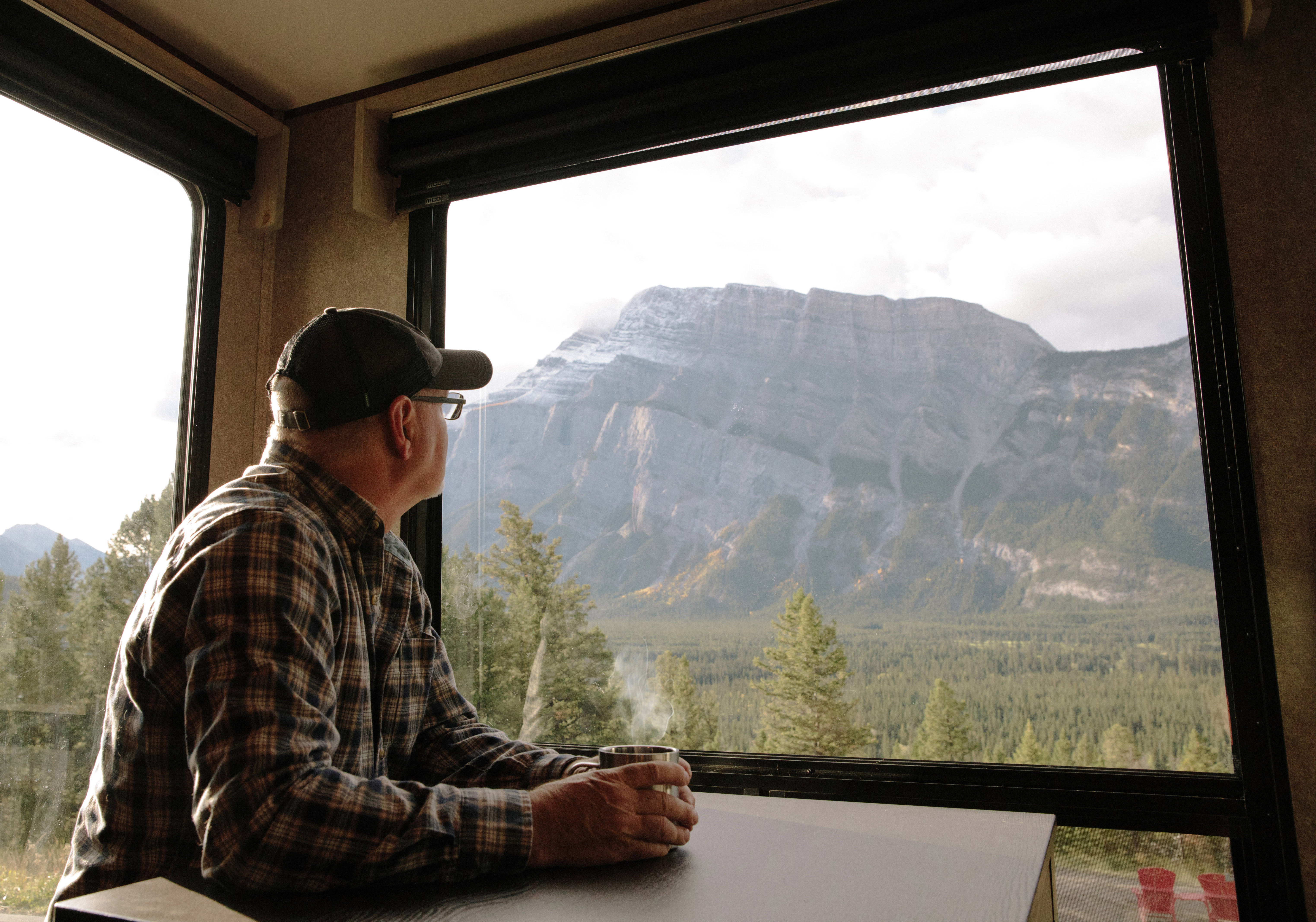 Craig Klinefelter enjoying a cup of coffee as he looks out the window at the mountains of Banff. 