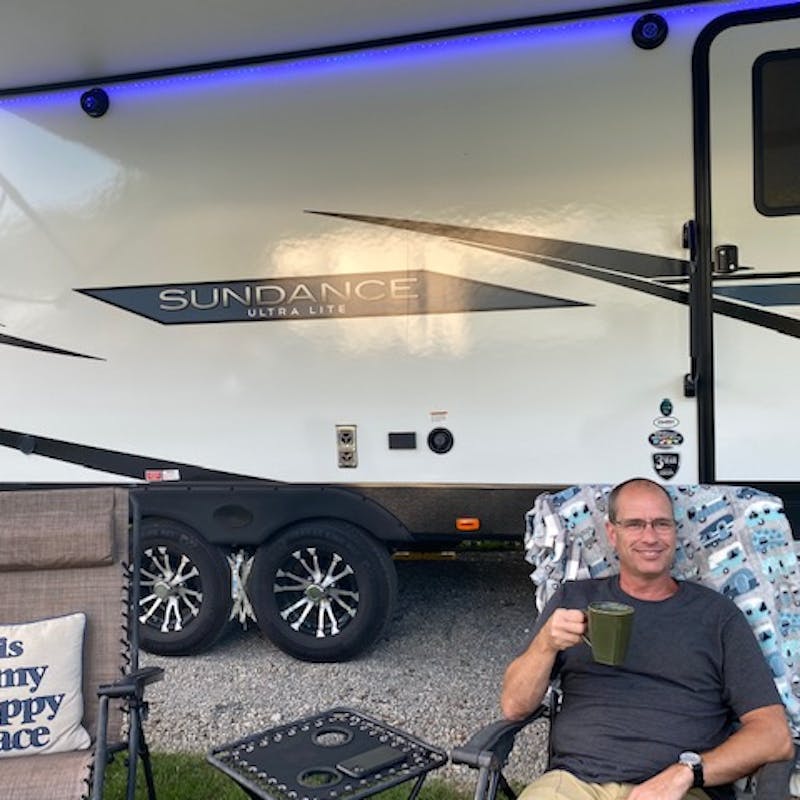 Matt Gleason sitting in a camping chair in front of his Sundance travel trailer