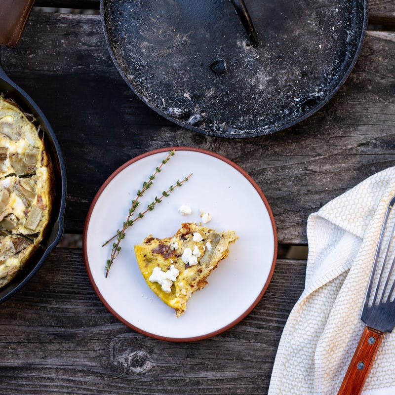 Cooked Bacon artichoke frittata in pan, with a piece of the frittata on a plate ready to eat.