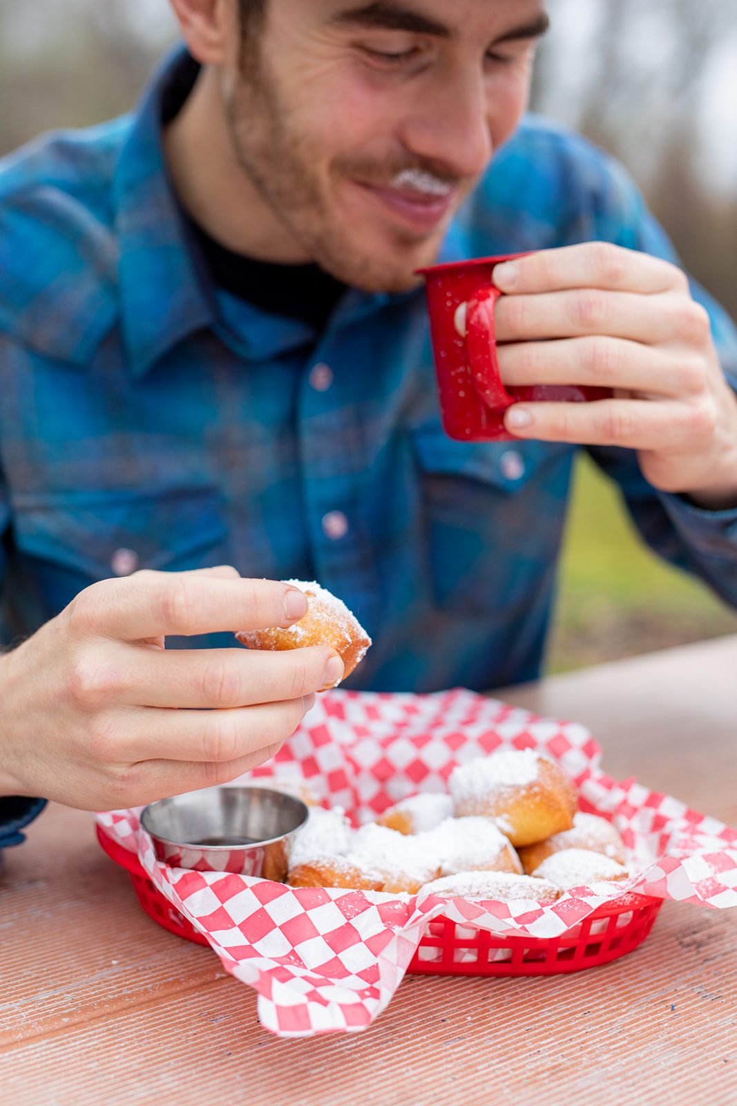 A man eating beignets and drinking a cup of coffee. 