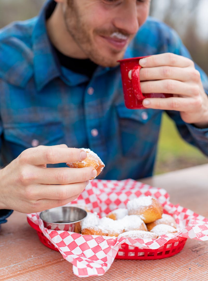A man eating beignets and drinking a cup of coffee.