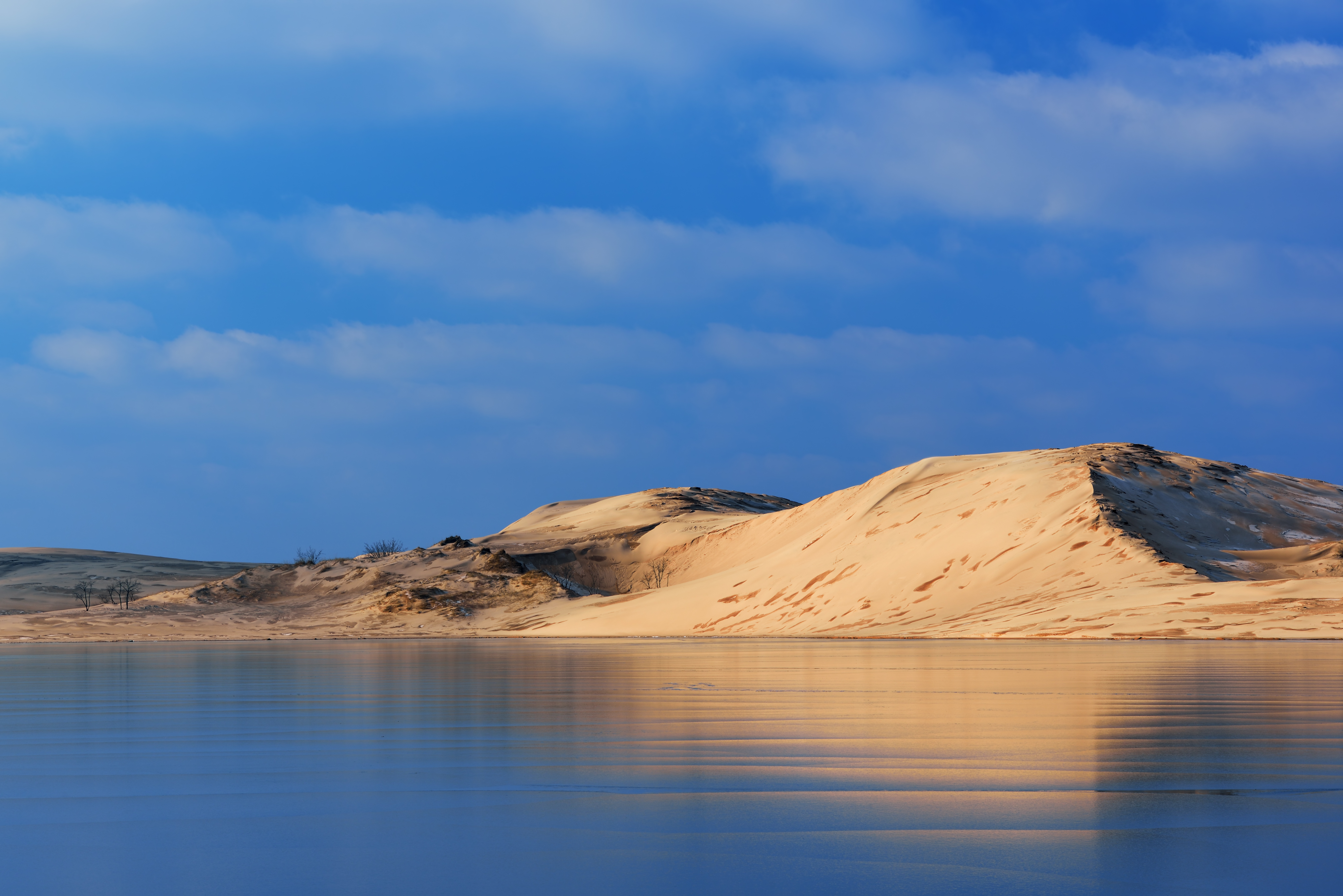 A sand dune reflects in a nearby lake. 