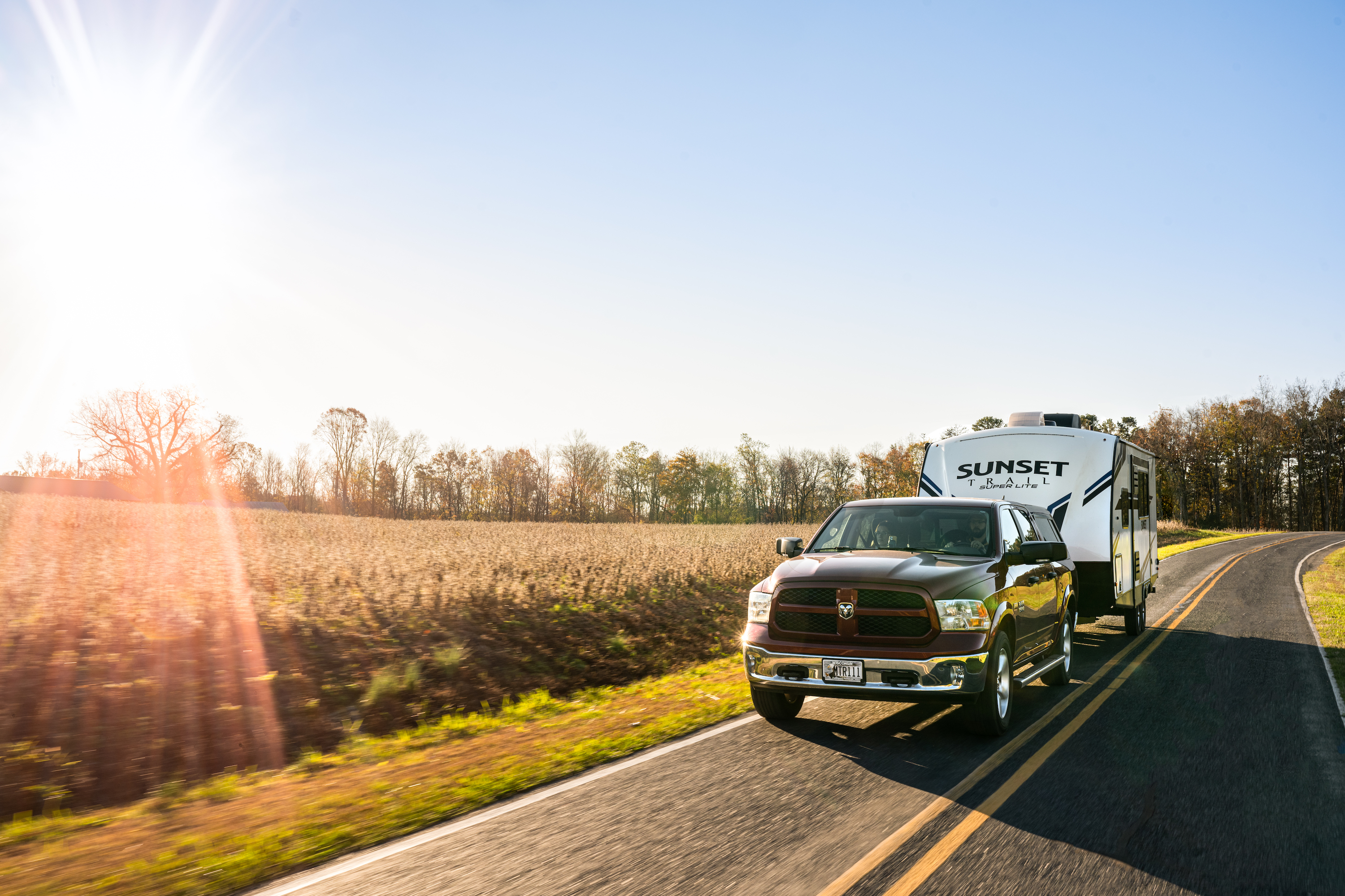 Todd & Marcia Schabel driving their Crossroads Sunset Travel Trailer down a road next to a field of crops.