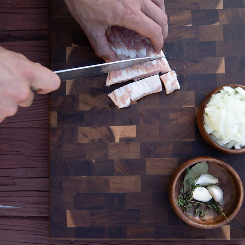 A top down view of hands cutting bacon on a cutting board.