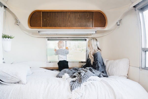 A woman and small child snuggled in blankets in an RV bed look out the window at a beautiful view