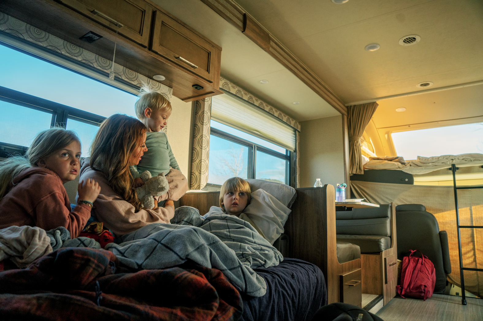 Mother snuggles with three kids inside RV on couch