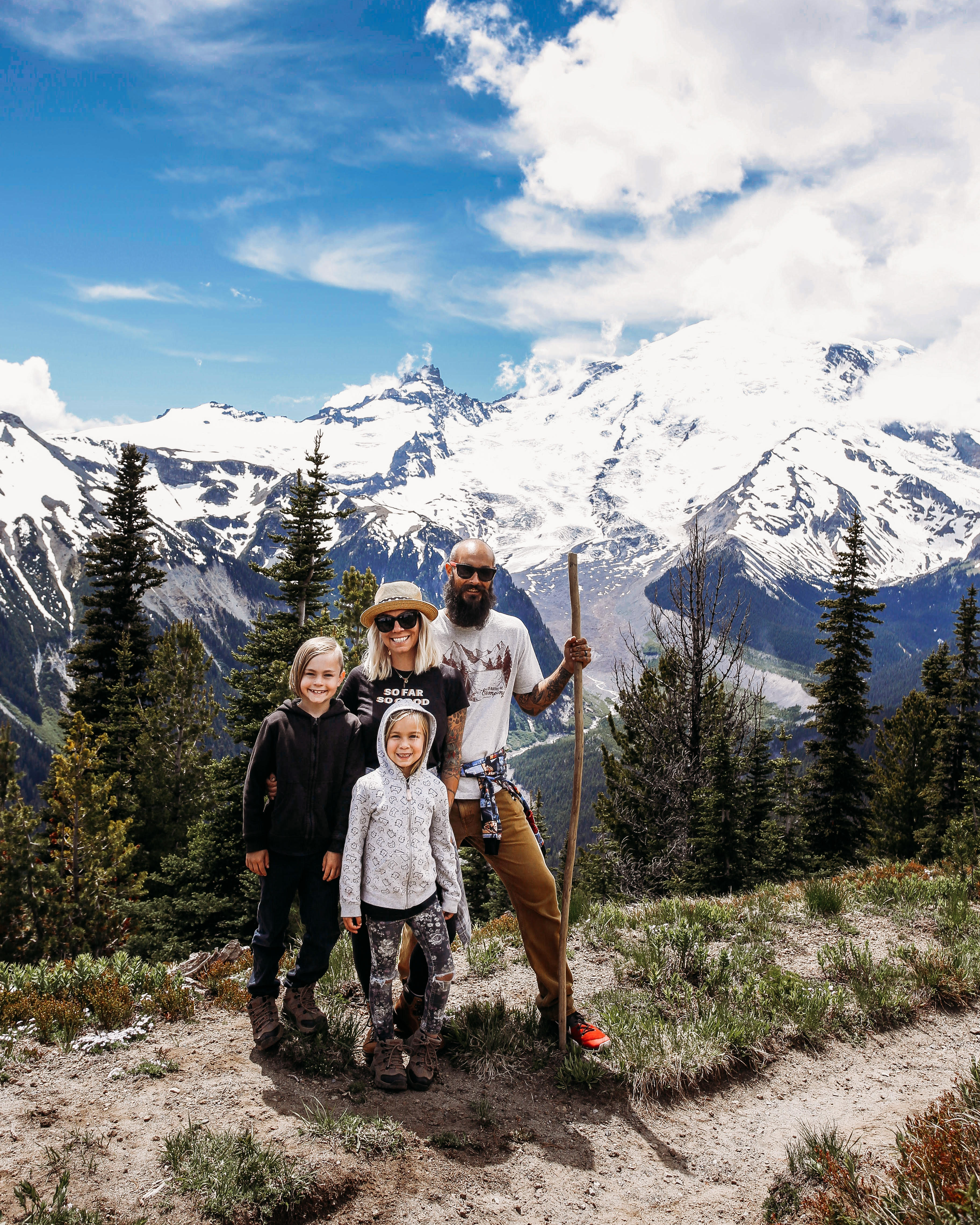 Michelle and Justin Russell with their two kids on a hike with beautiful snow-capped mountain peaks and blue skies