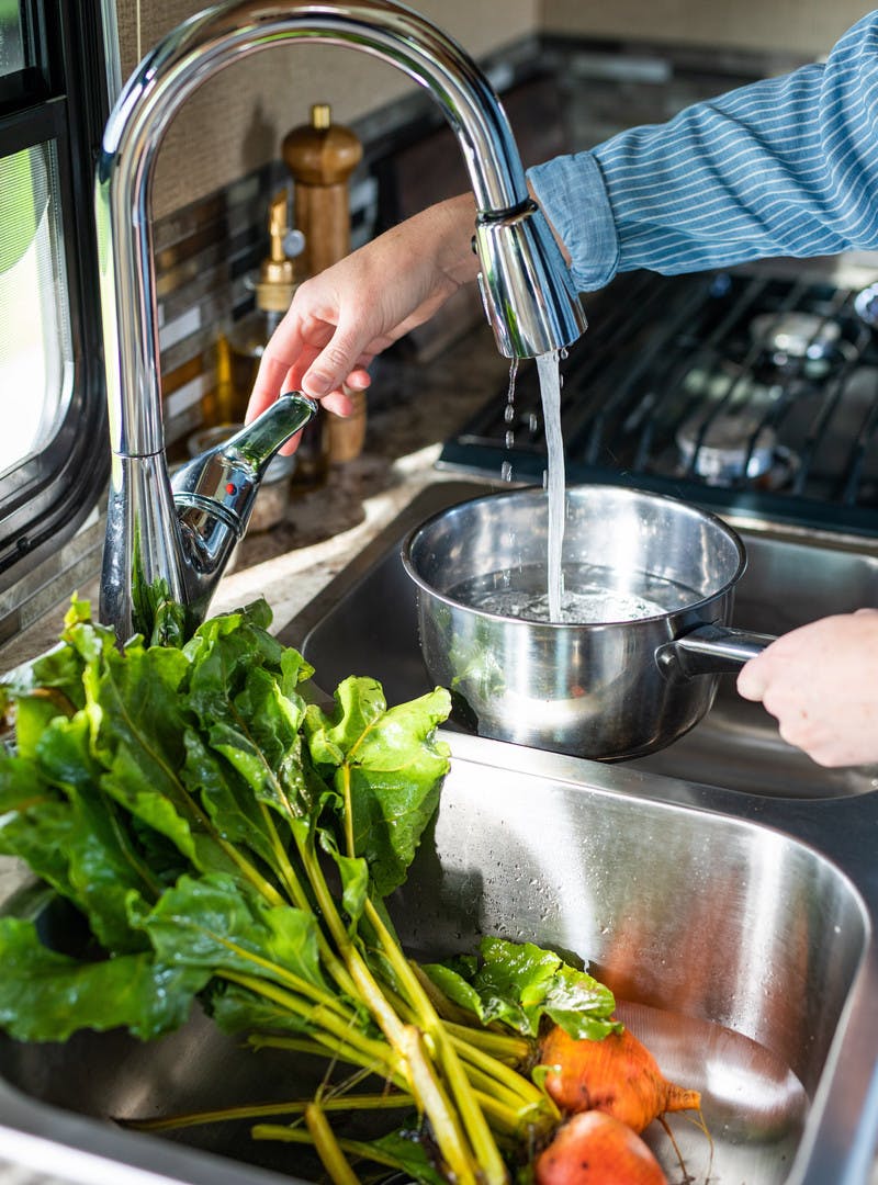 Faucet filling a pot of water while orange beets rest inside stainless steel sink.