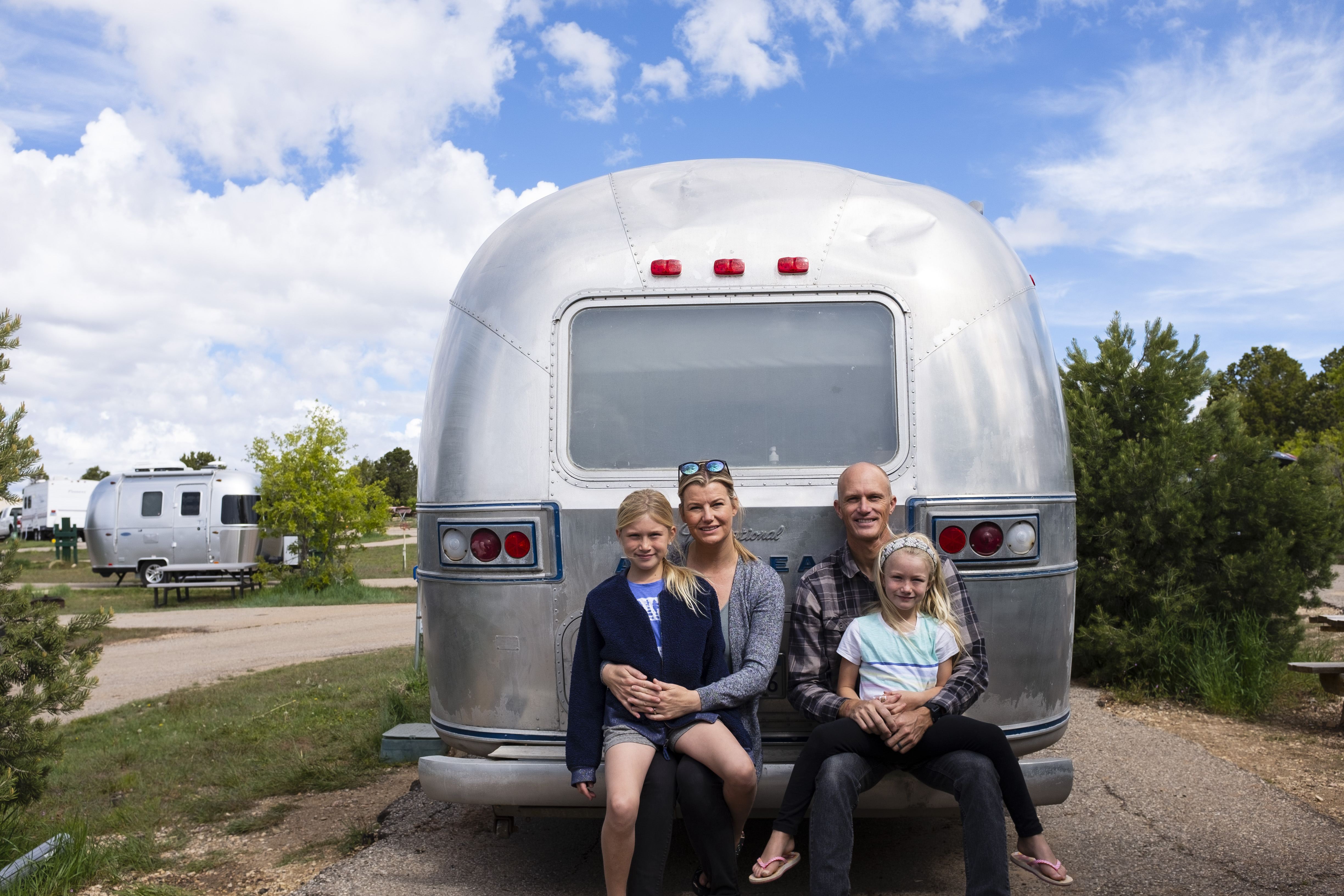 A family of four posed for a photo, sitting on the back bumper of their Airsteram. 