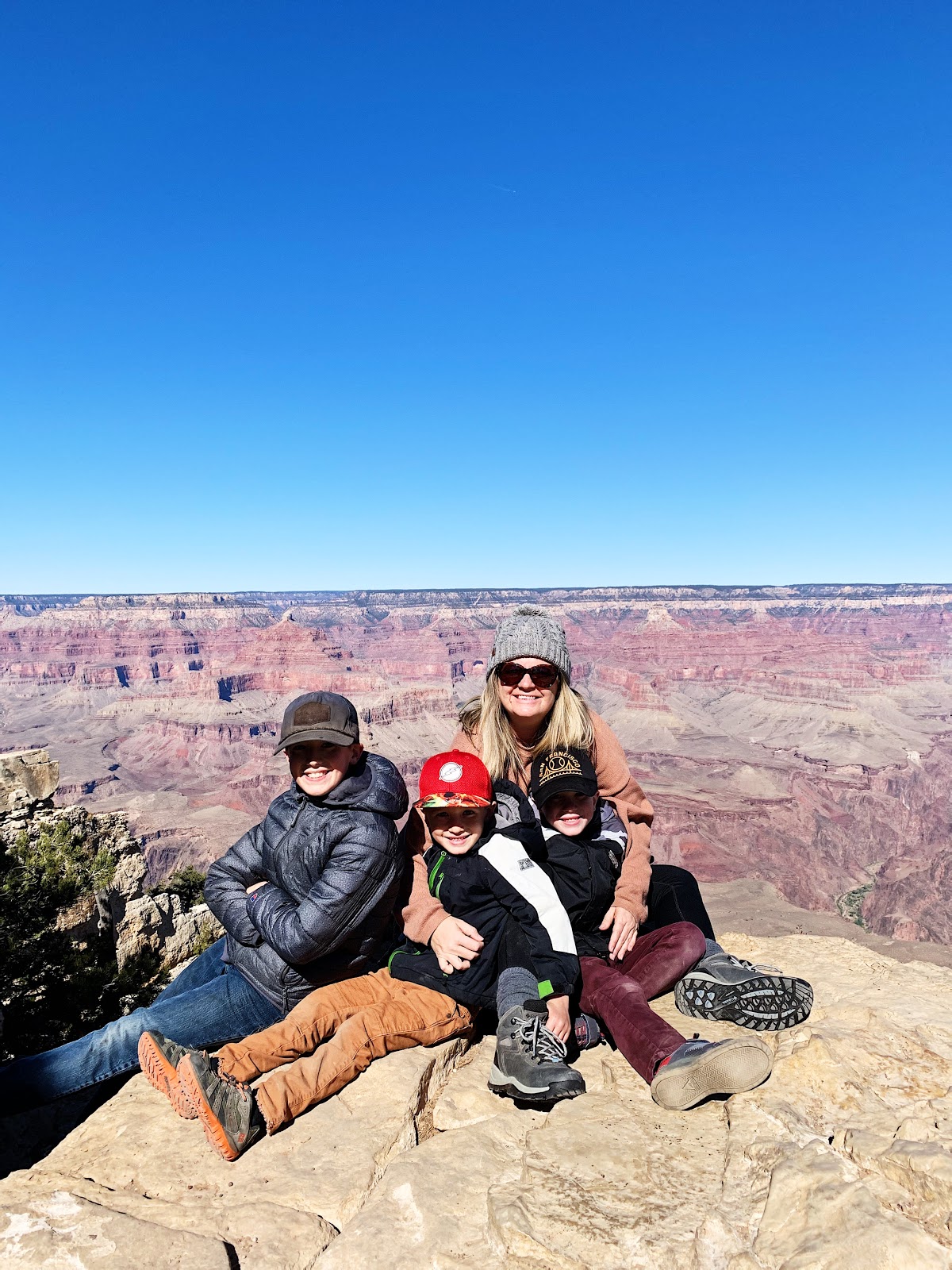 A mom and three boys posed for a picture  in front of the Grand Canyon.