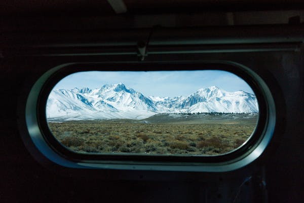 Snowy mountain peaks in the distance, seen through an oblong, rounded RV window. 