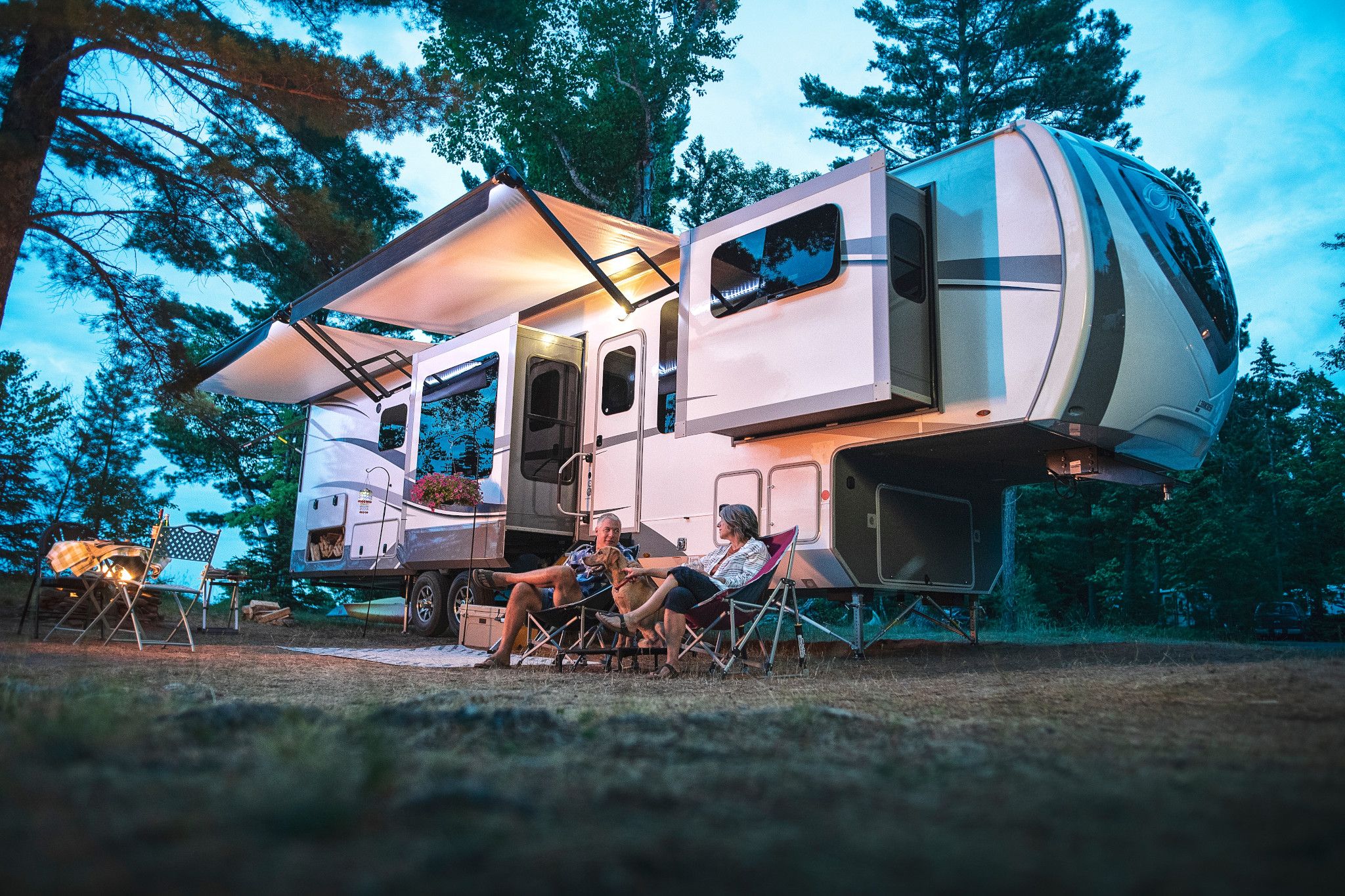 A couple sitting in camp chairs in front of a fifth wheel RV