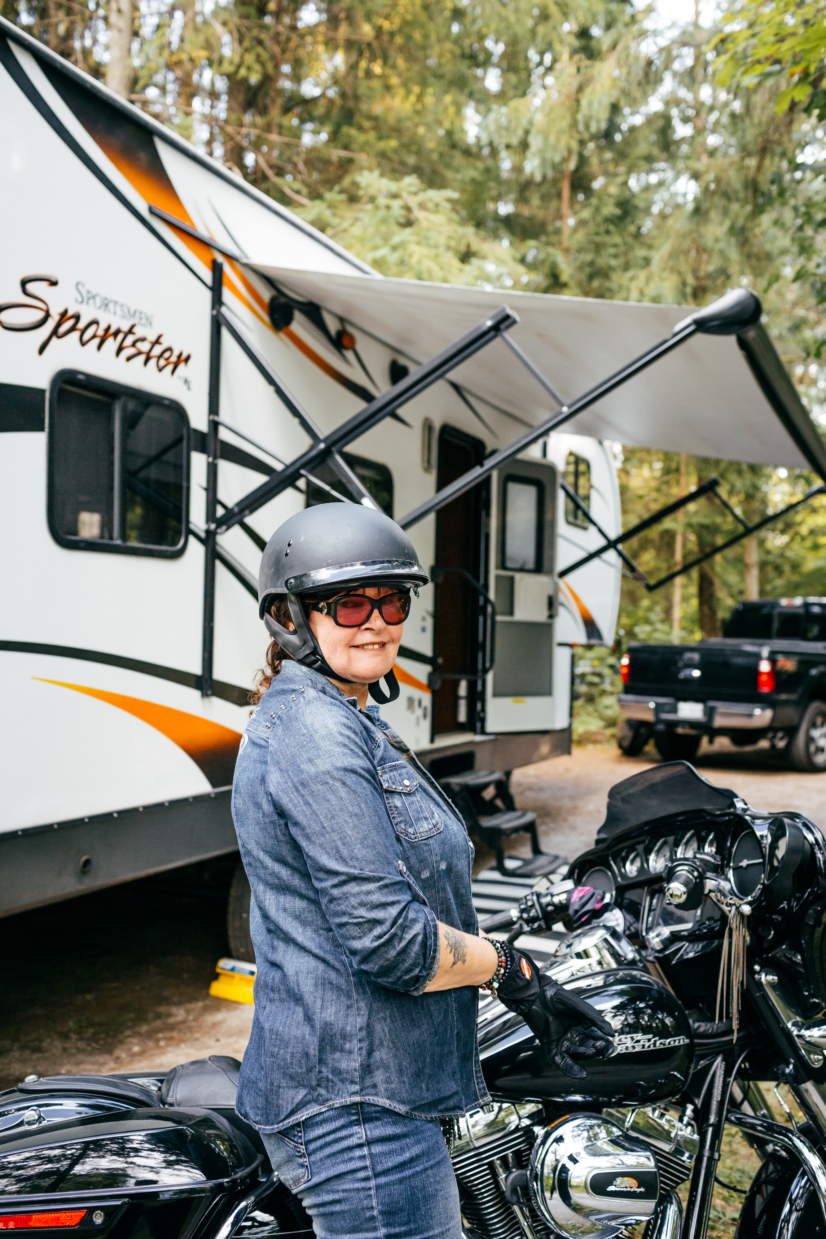 A woman smiles as she sits idle on her motorcycle in front of her toy hauler RV.