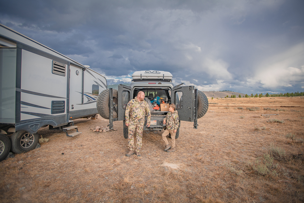 Nate Day and his son in hunting gear stand outside of a truck next to an RV.