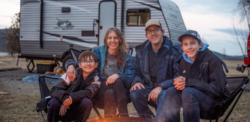 The Takacs family sitting around a bonfire with their Jayco Jay Flight in the background.