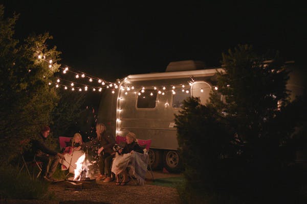 Family sitting around fire in front of Airstream, hung lights.