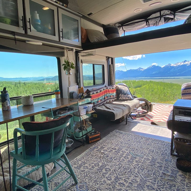 Amy Rekart's Cruiser Stryker toy hauler's back patio opens up to a beautiful mountain scene with lush grass and sunny skies.