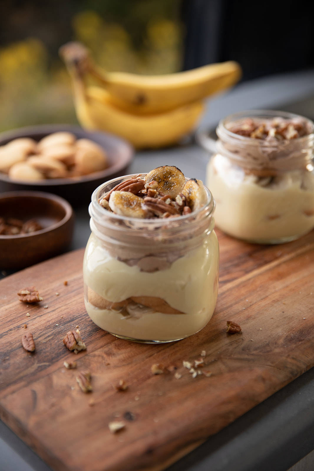 Beautifully layered pudding parfaits in glass jars on top of a wooden cutting board. 