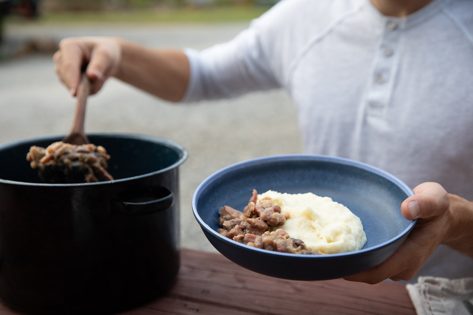 A man ladling beans into a bowl on top of mashed potatoes. 