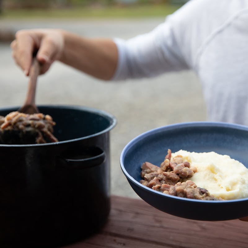 A man ladling beans into a bowl on top of mashed potatoes.