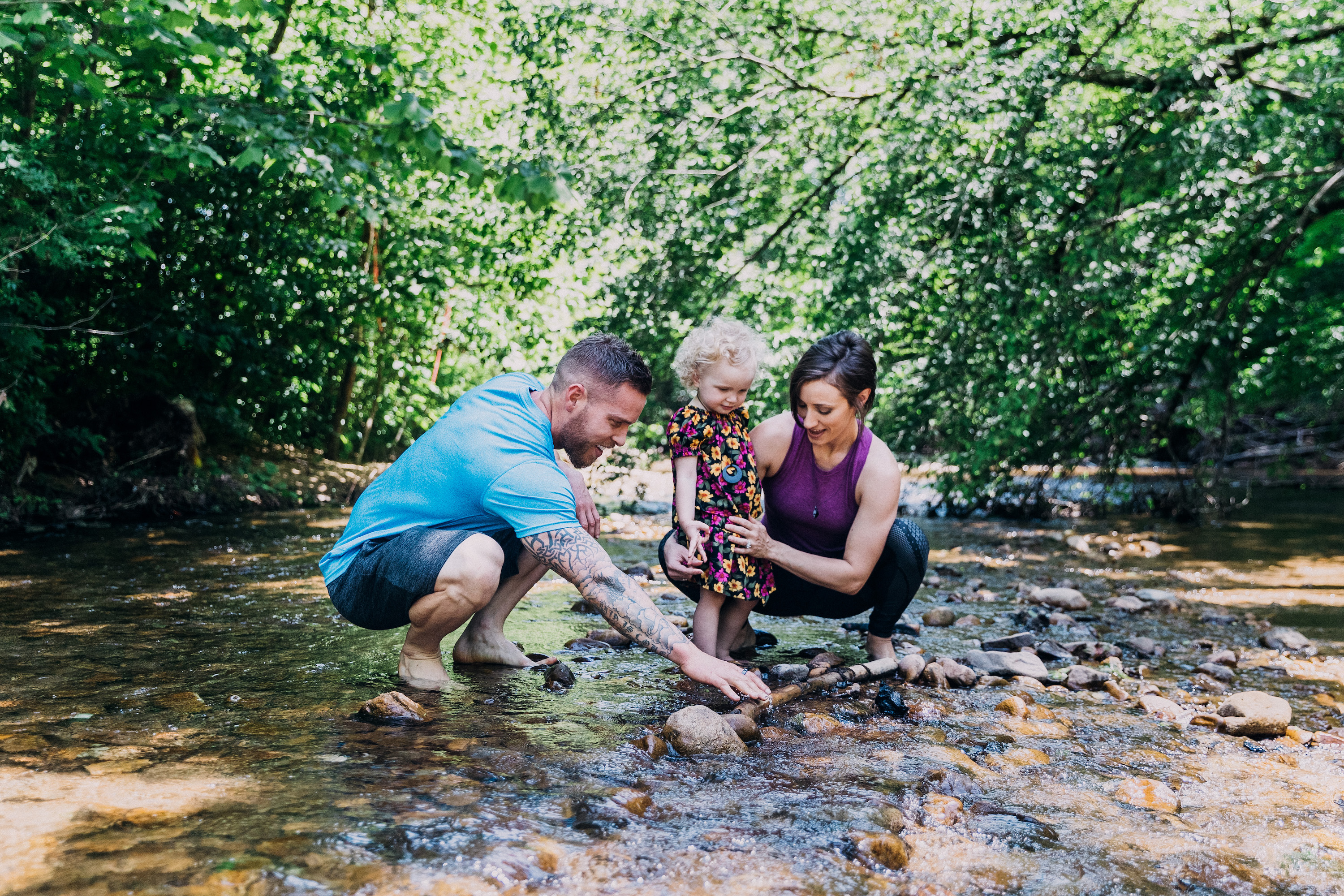A mom, dad and young daughter playing in a shallow stream. 
