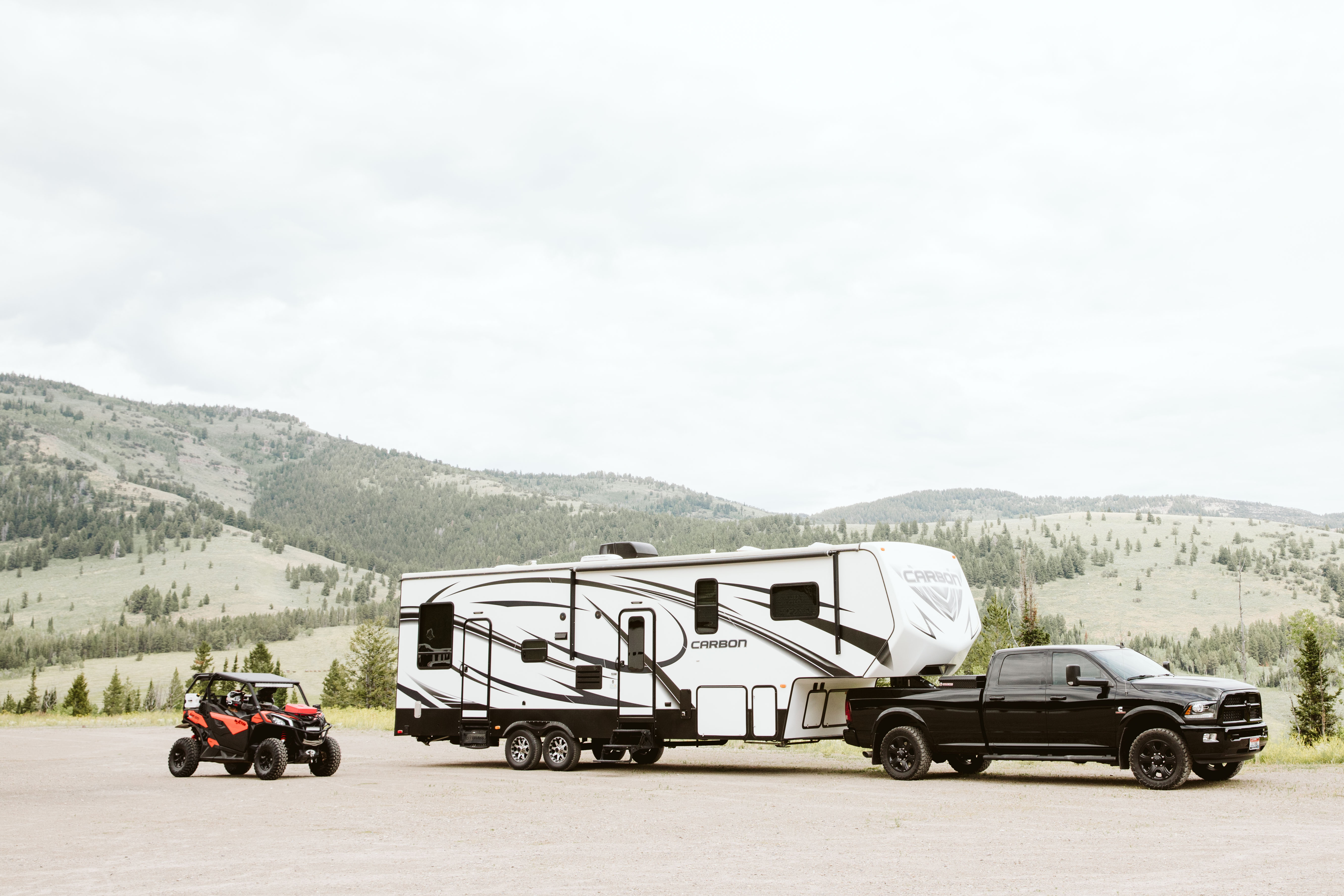 A fifth wheel toy hauler RV parked next to a side by side. 