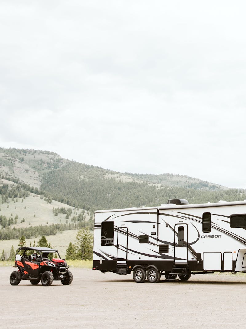 A fifth wheel toy hauler RV parked next to a side by side. 