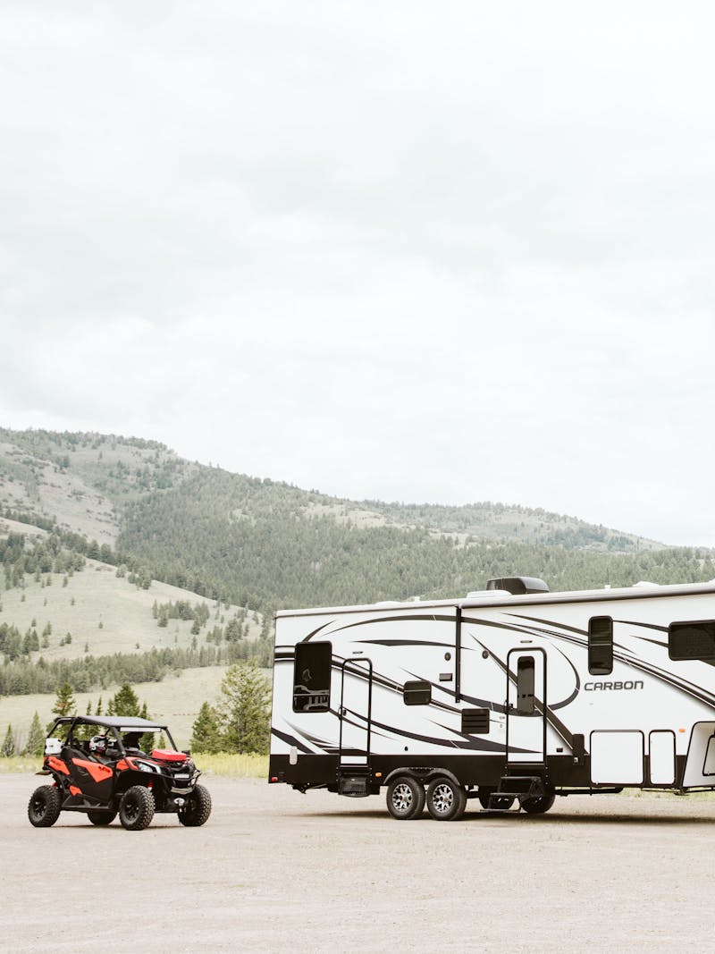 A fifth wheel toy hauler RV parked next to a side by side.