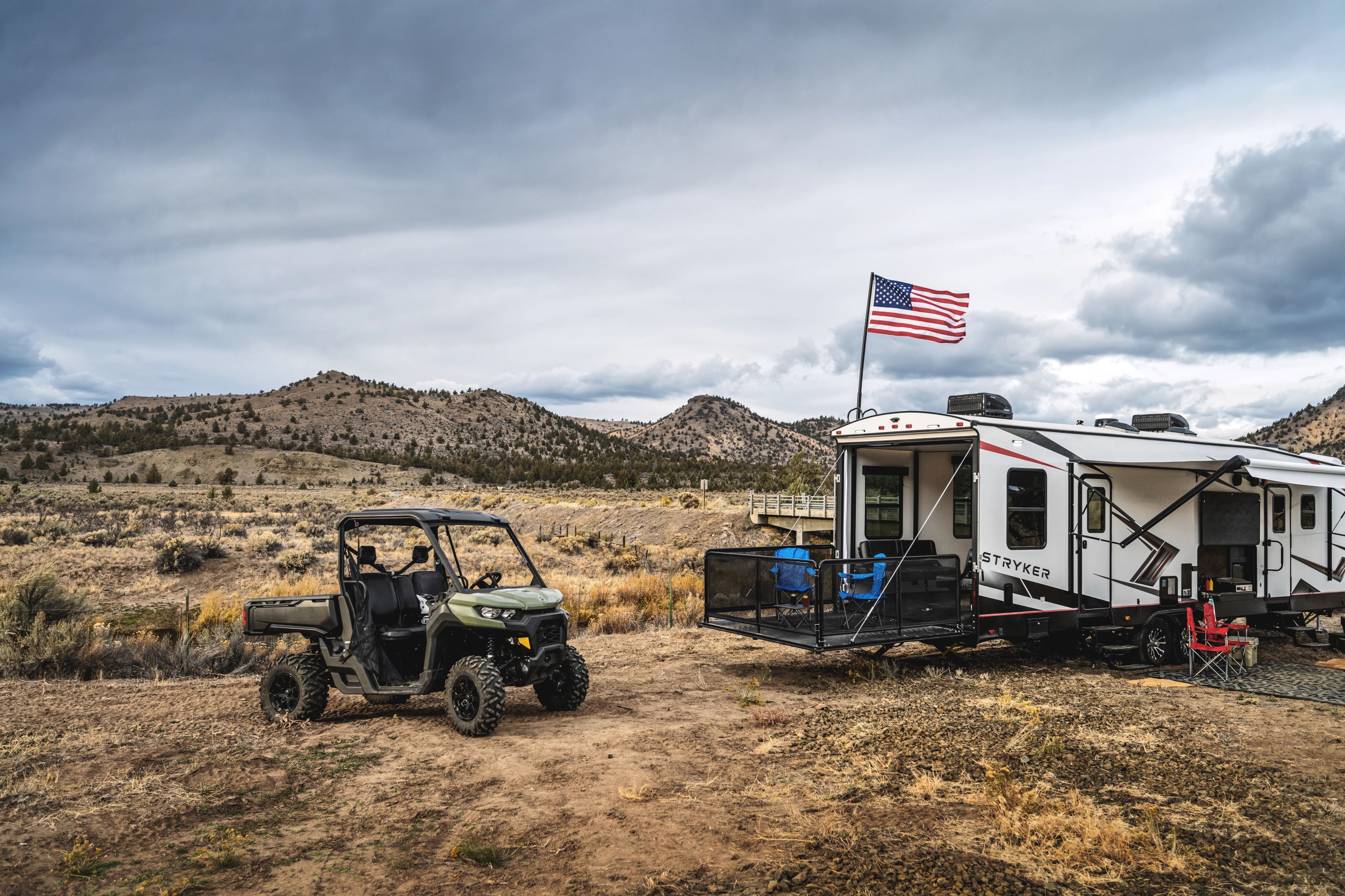 a toy hauler RV with an american flag attached to it and a 4x4 vehicle parked next to it