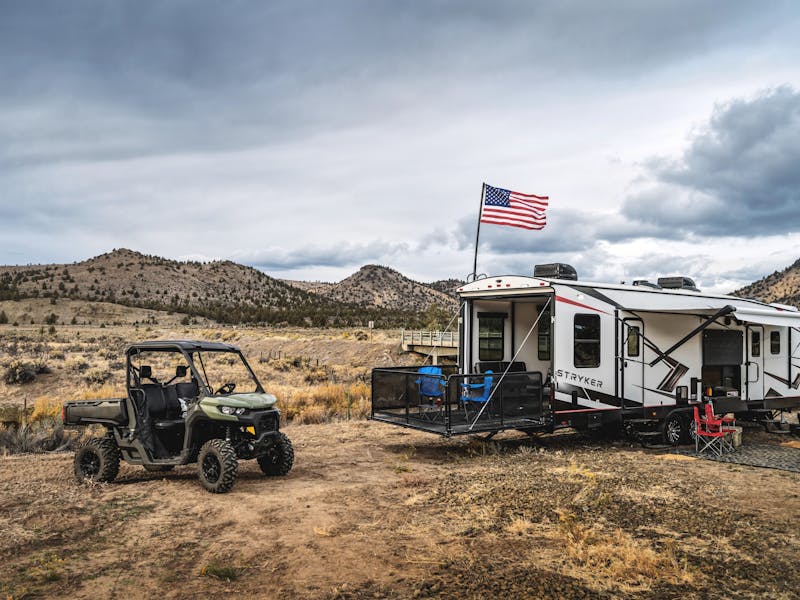 a toy hauler RV with an american flag attached to it and a 4x4 vehicle parked next to it
