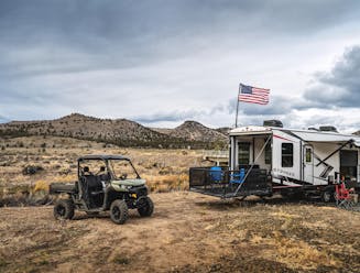 a toy hauler RV with an american flag attached to it and a 4x4 vehicle parked next to it