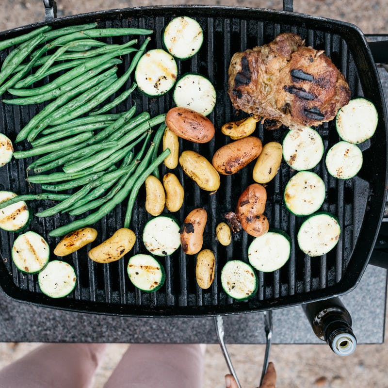 Aerial shot of green beans, potatoes, vegetables, and pork on a grill.