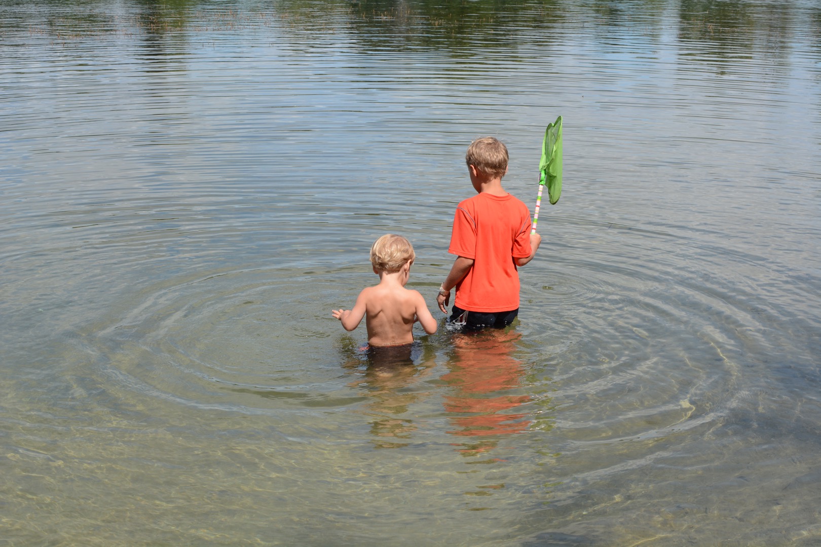 Two young boys wading into clear water. 