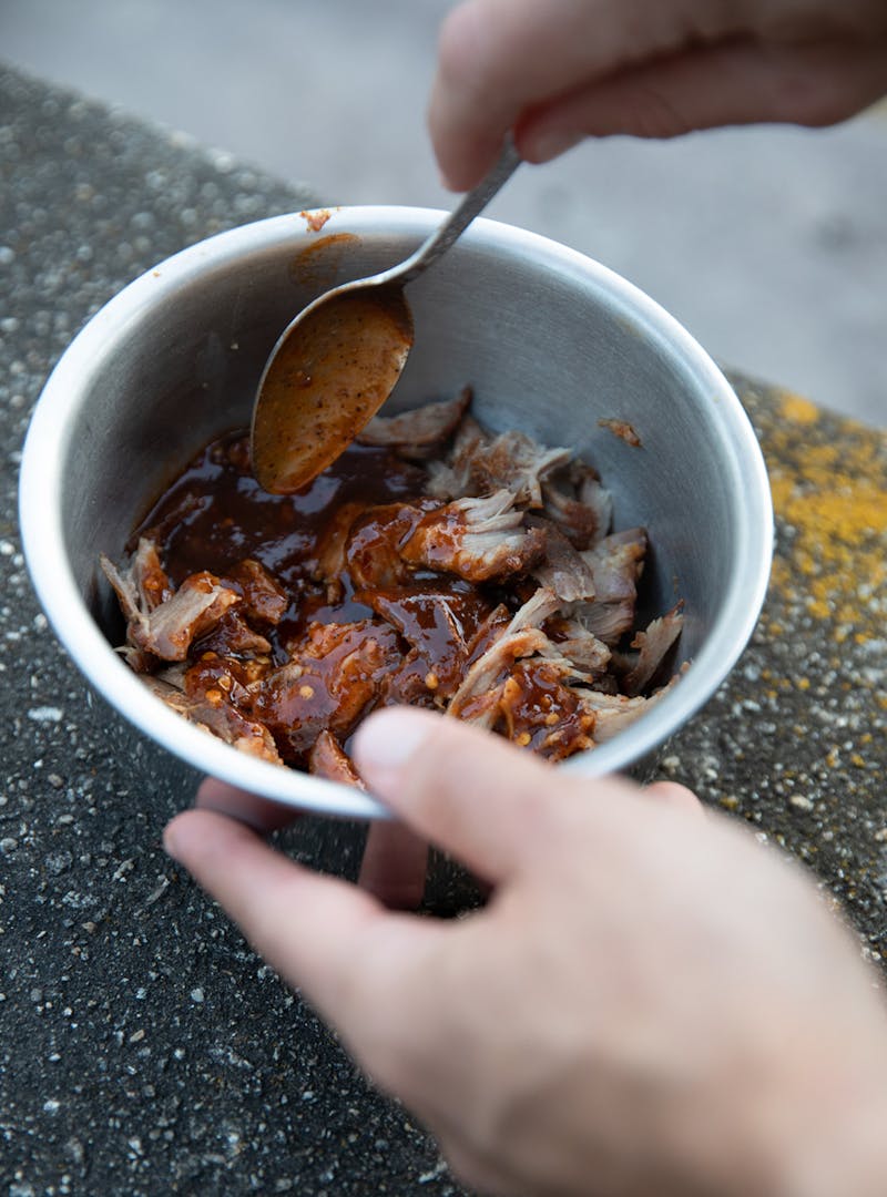 Pulled pork in a bowl gets mixed with barbeque sauce.