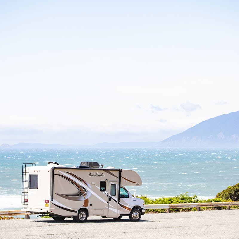 Class-C motorhome in front of ocean beach, along road, with mountain in the fog.