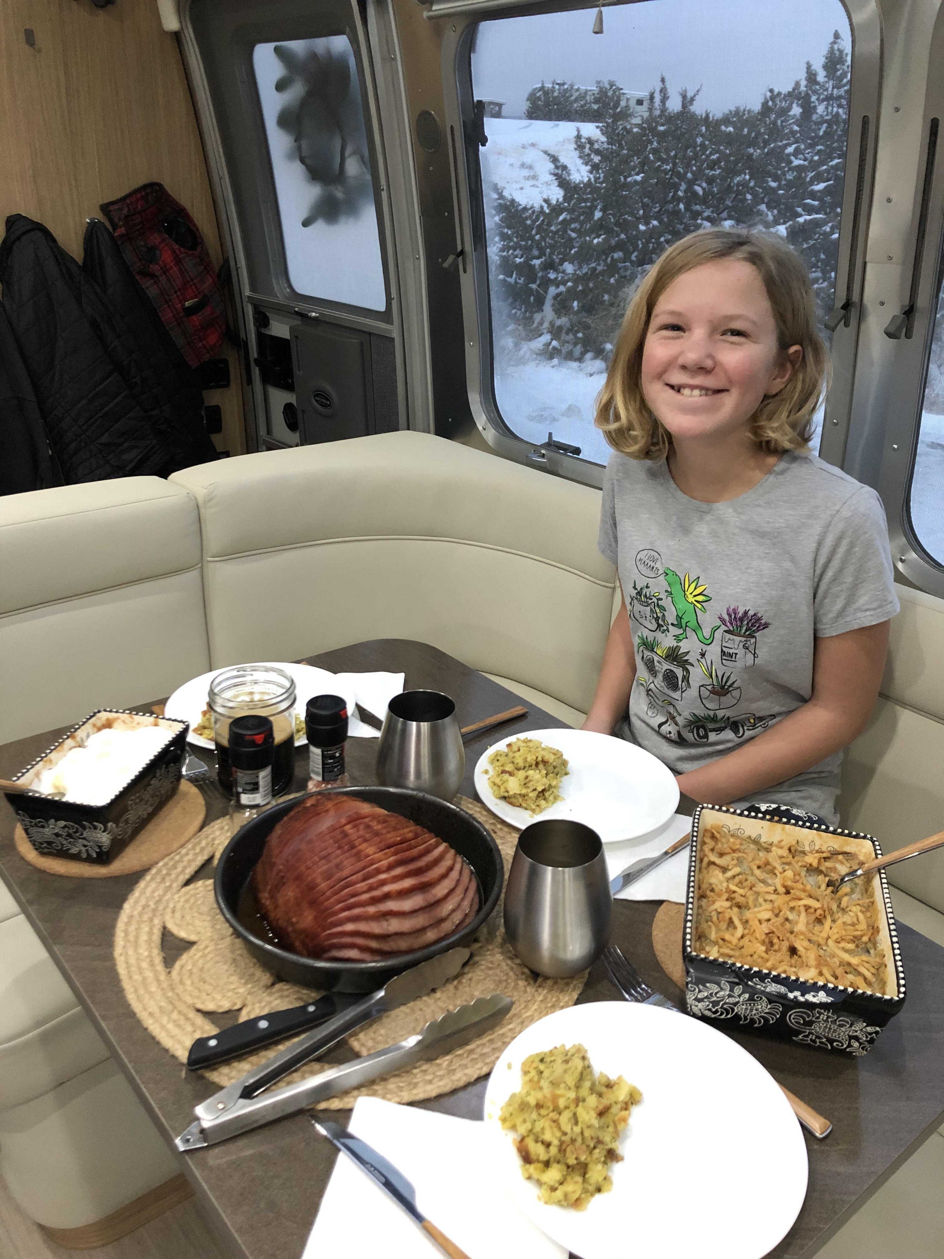 Karen Blue's daughter eating thanksgiving dinner inside their Airstream with a snowy landscape outside the window