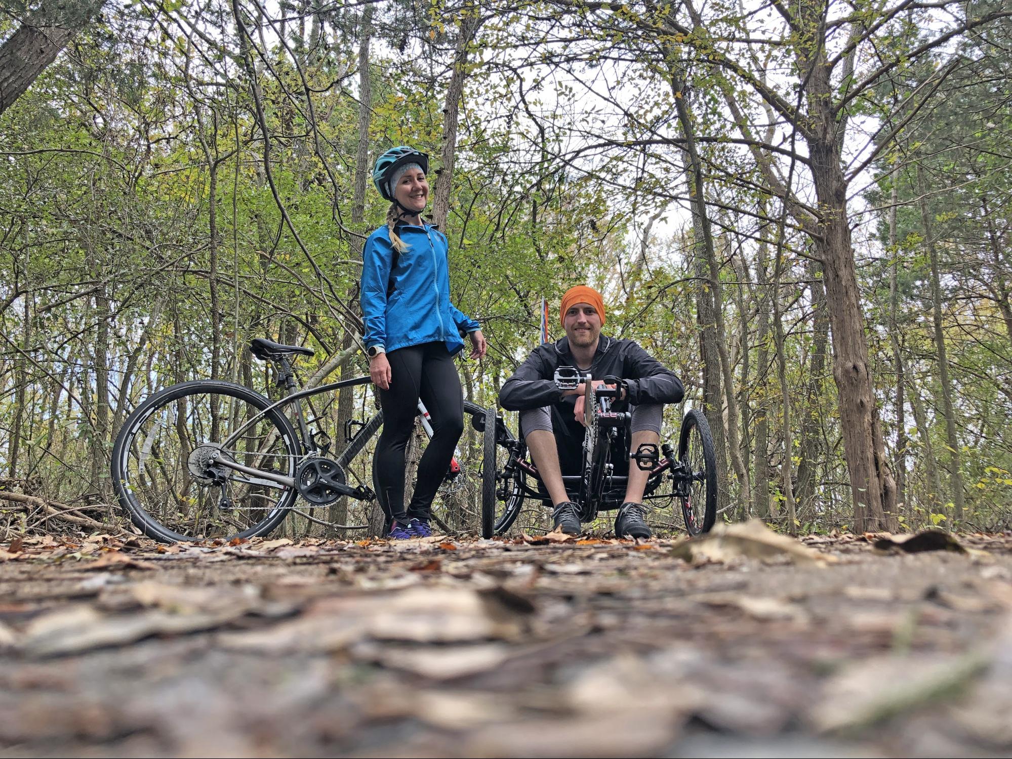 A woman and her husband in a forest with their mountain bikes.