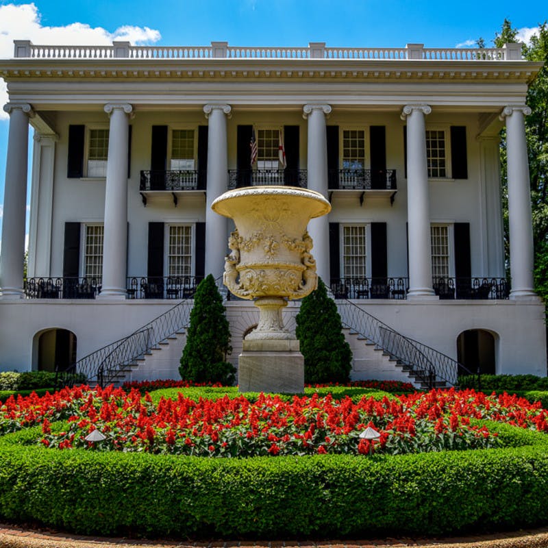 The President's Mansion Greek Revival white mansion at University of Alabama in Tuscaloosa, Alabama, with large fountain and red flowers.