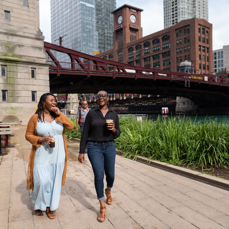Chanel and Brittany Tate walking along the Chicago riverfront drinking coffee and talking.