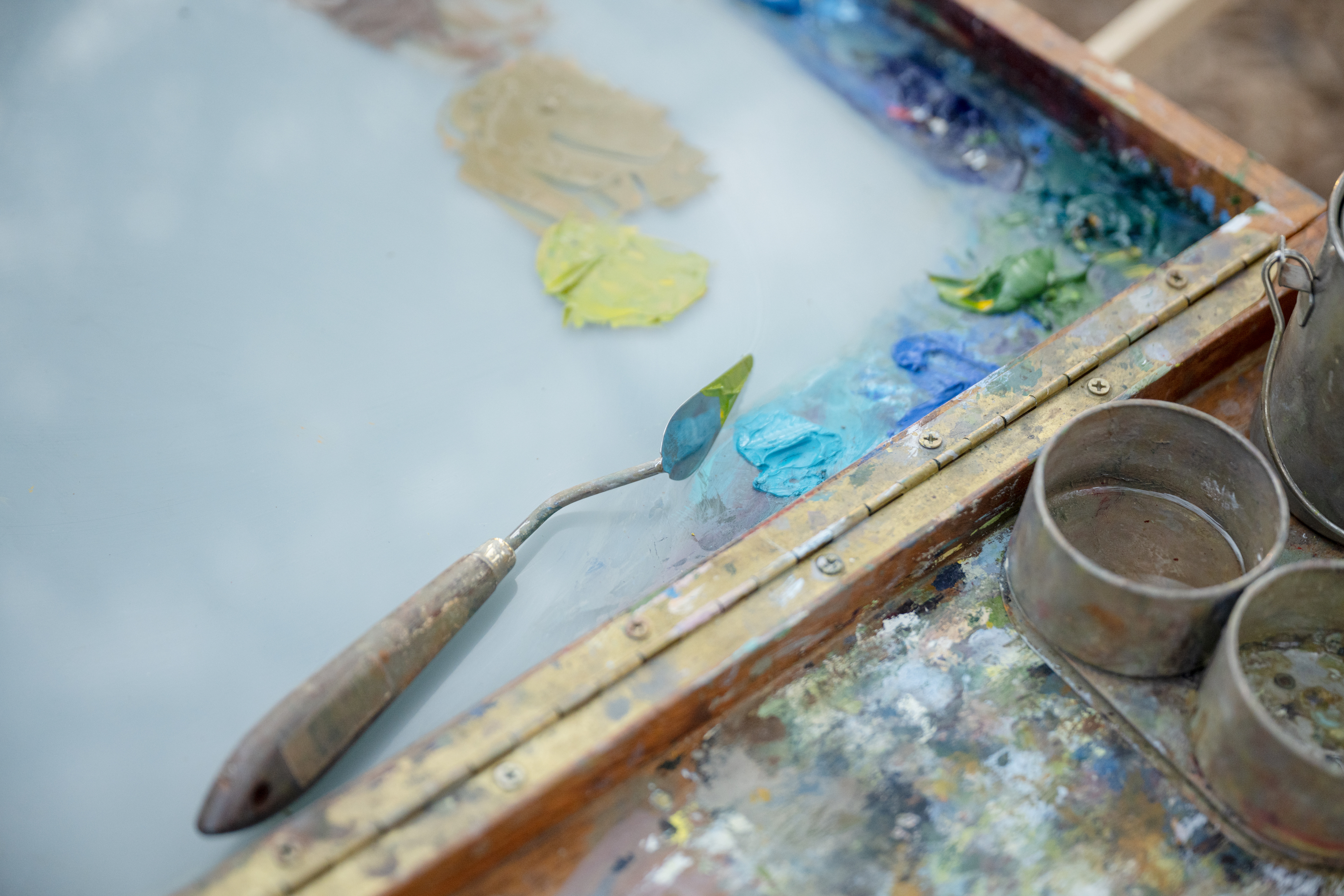 A board with blue, green and yellow paint used to paint a landscape. 