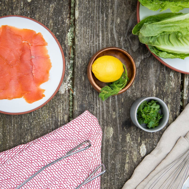 Prepped ingredients on a picnic table, including lox, lemon and dill, lettuce, and parsley. 