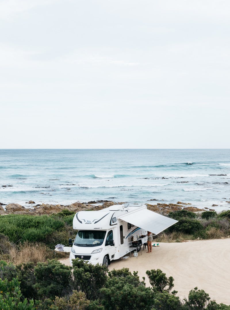 A Class C motorhome parked on the beach next to the ocean with a beautiful view.