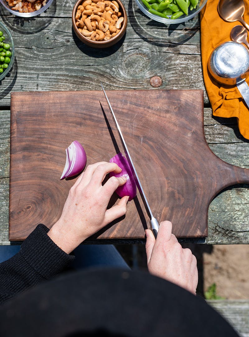 Above shot of hands slicing red onion on cutting board, with small glass bowls around.