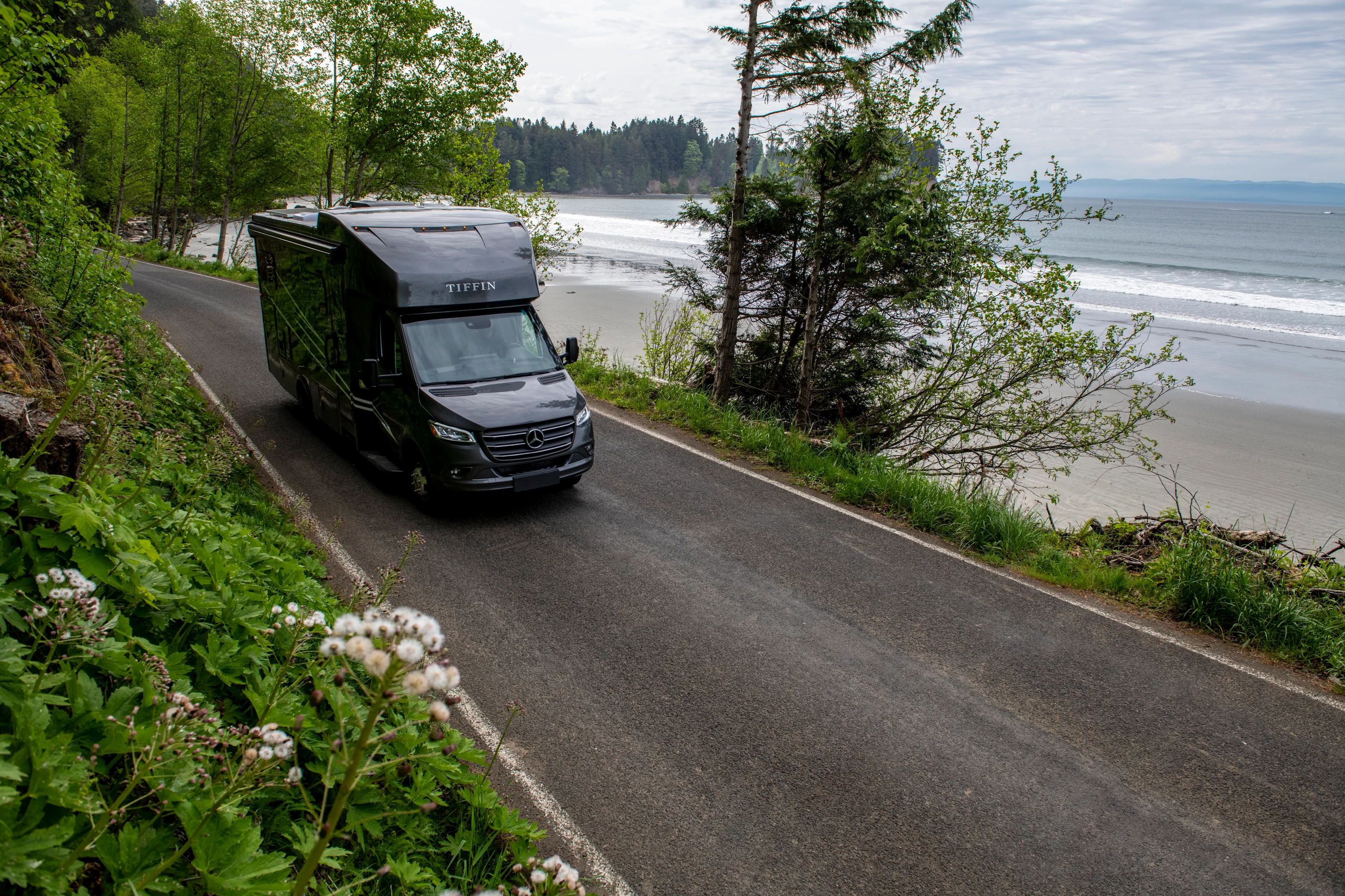 A tiffin wayfarer class C rv driving down the road next to the ocean
