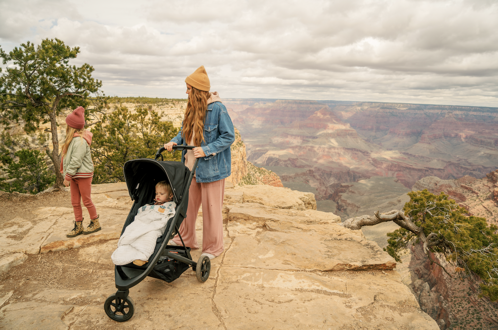 Women in yellow hat pushes stroller with little girl standing next to her on edge near Grand Canyon