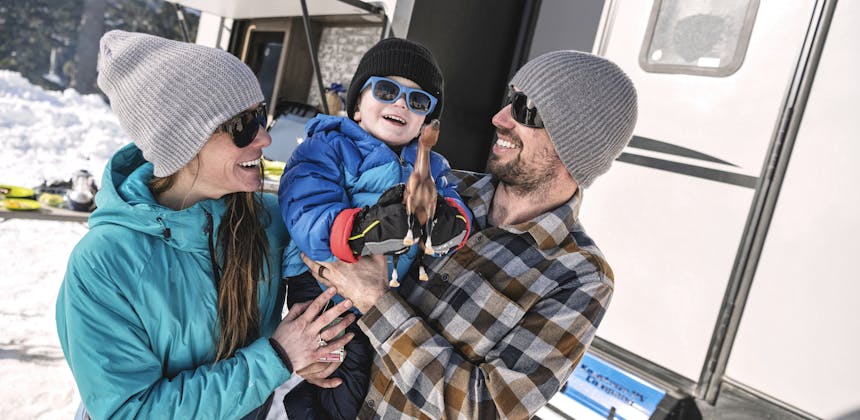 A mother and father hold up their young son who holds a toy horse in front of an RV.
