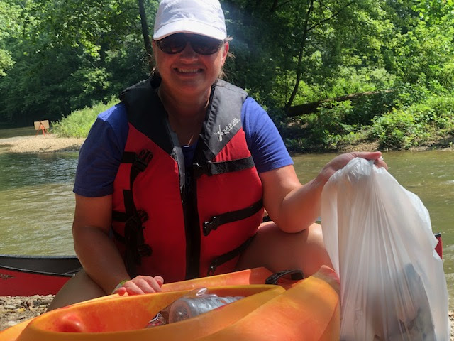 A middle aged woman in a kayak holding a bag of litter she's gathered. 