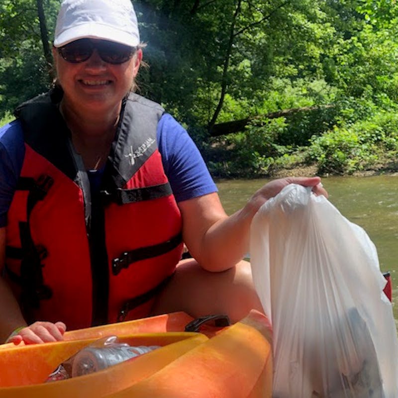A middle aged woman in a kayak holding a bag of litter she's gathered.