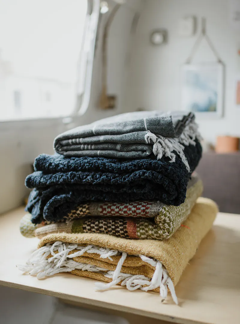 Pile of blue, yellow, and multi colored blankets stacked on top of each other on a table.