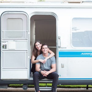 Image of Christina and Mack Griffin sitting in the doorway of their Airstream Travel Trailer RV. 